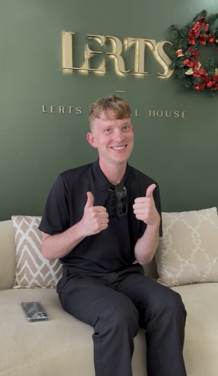 Smiling patient giving two thumbs up at the LERTS Dental House logo wall, Chiang Mai